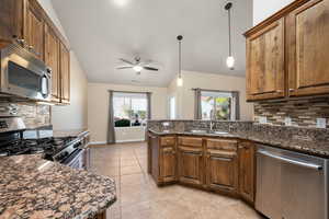 Kitchen with tasteful backsplash, stainless steel appliances, dark stone counters, pendant lighting, and lofted ceiling