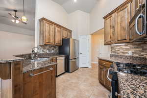 Kitchen featuring stainless steel appliances, dark stone countertops, ceiling fan, a peninsula, and light tile patterned floors