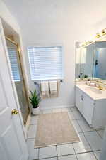Full bathroom featuring vanity, light tile patterned flooring, a shower stall, and a textured ceiling. AI decor.