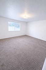 Primary bedroom. Carpeted empty room with a textured ceiling and baseboards