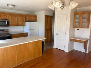 Kitchen with wood finish cabinetry, stainless steel appliances, light countertops, and dark wood-style flooring
