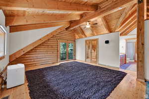 Bonus room with french doors, rustic walls, wooden ceiling, light wood-style flooring, and lofted ceiling with beams
