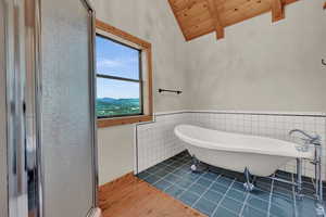 Full bath featuring tile walls, wainscoting, wood ceiling, pet washing area, and lofted ceiling with beams