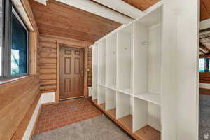 Mudroom featuring wood ceiling, dark carpet, and log walls