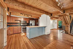 Kitchen with rail lighting, a wooden ceiling with exposed beams, a kitchen breakfast bar, stainless steel appliances, and wood finish cabinetry