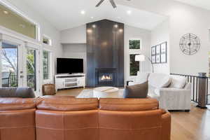 Living room featuring a high ceiling, light wood-type flooring, a ceiling fan, and a fireplace