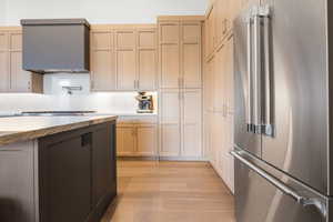 Kitchen with high end fridge, range hood, light stone counters, light wood-type flooring, and two tone cabinetry