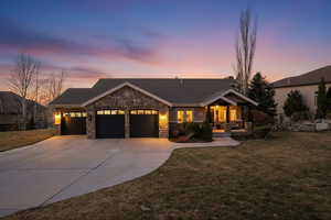 View of front of property with a front yard, an attached garage, stone siding, covered porch, and concrete driveway