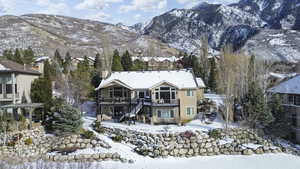 Snow covered back of property featuring a mountain view, a balcony, a patio, and stucco siding