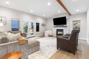 Living area with a glass covered fireplace, light wood-type flooring, recessed lighting, and beamed ceiling