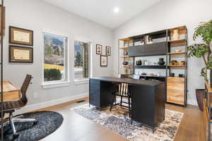 Office with light wood-style floors and vaulted ceiling