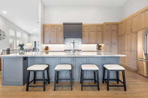 Kitchen featuring a kitchen bar, light stone countertops, light wood-type flooring, high quality fridge, and a large island