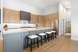 Kitchen with high quality fridge, light stone counters, light wood-type flooring, lofted ceiling, and a spacious island