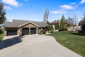 View of front facade featuring a shingled roof, a front yard, an attached garage, driveway, and stone siding