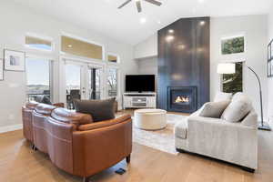 Living area featuring healthy amount of natural light, light wood-type flooring, vaulted ceiling, a fireplace, and ceiling fan