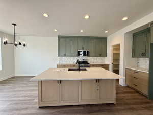 Kitchen with decorative backsplash, light stone counters, green cabinetry, dark wood-type flooring, and stainless steel appliances