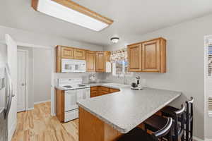 Kitchen featuring a breakfast bar, a peninsula, white appliances, light wood-style floors, and light countertops