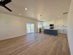 Kitchen with open floor plan, hanging lights, light countertops, a kitchen island, and two tone cabinetry