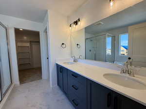 Full bathroom with double vanity, a walk in closet, a shower stall, and light marble finish flooring