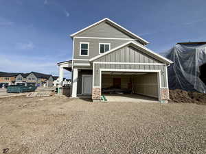 View of front of home with board and batten siding, a patio, a garage, gravel driveway, and brick siding