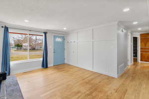 Foyer entrance featuring light wood-type flooring, crown molding, recessed lighting, and a textured ceiling