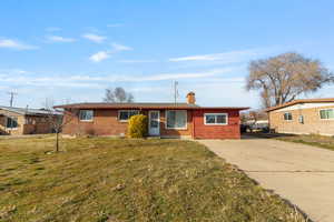 Single story home with a chimney, concrete driveway, brick siding, and a front yard