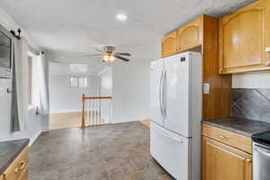 Kitchen featuring freestanding refrigerator, a textured ceiling, a ceiling fan, tile countertops, and ornamental molding