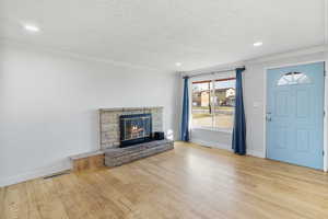 Unfurnished living room featuring light wood-style flooring, a glass covered fireplace, ornamental molding, recessed lighting, and a textured ceiling