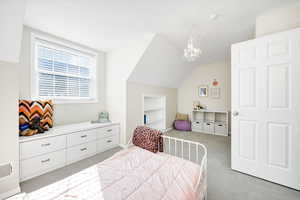 Bedroom featuring lofted ceiling, light carpet, and a chandelier