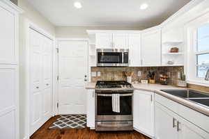 Kitchen with open shelves, stainless steel appliances, white cabinets, light countertops, and recessed lighting