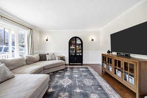 Living room featuring wainscoting, dark wood-style floors, a decorative wall, and crown molding
