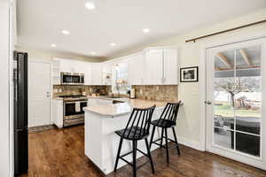 Kitchen featuring open shelves, a peninsula, stainless steel appliances, light countertops, and a breakfast bar
