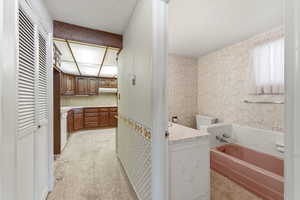 Full bath with wallpapered walls, a bath, vanity, light colored carpet, and a closet