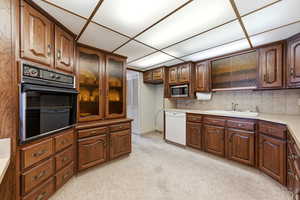 Kitchen featuring black oven, white dishwasher, light carpet, light countertops, and stainless steel microwave