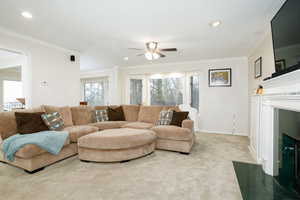 Carpeted living area featuring a fireplace with flush hearth, a ceiling fan, crown molding, and recessed lighting