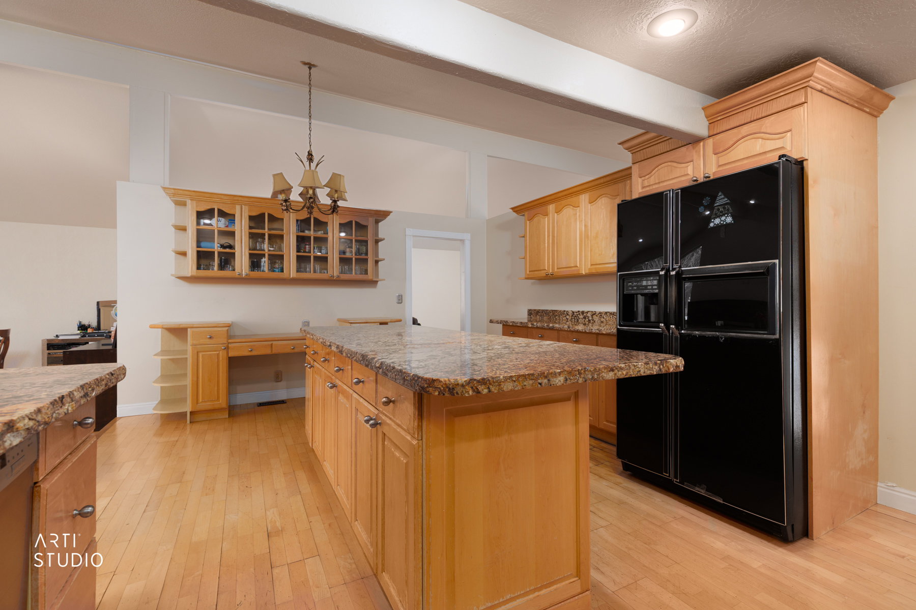 Kitchen featuring black fridge with ice dispenser, light wood finish cabinets, light wood-type flooring, glass insert cabinets, and a kitchen island