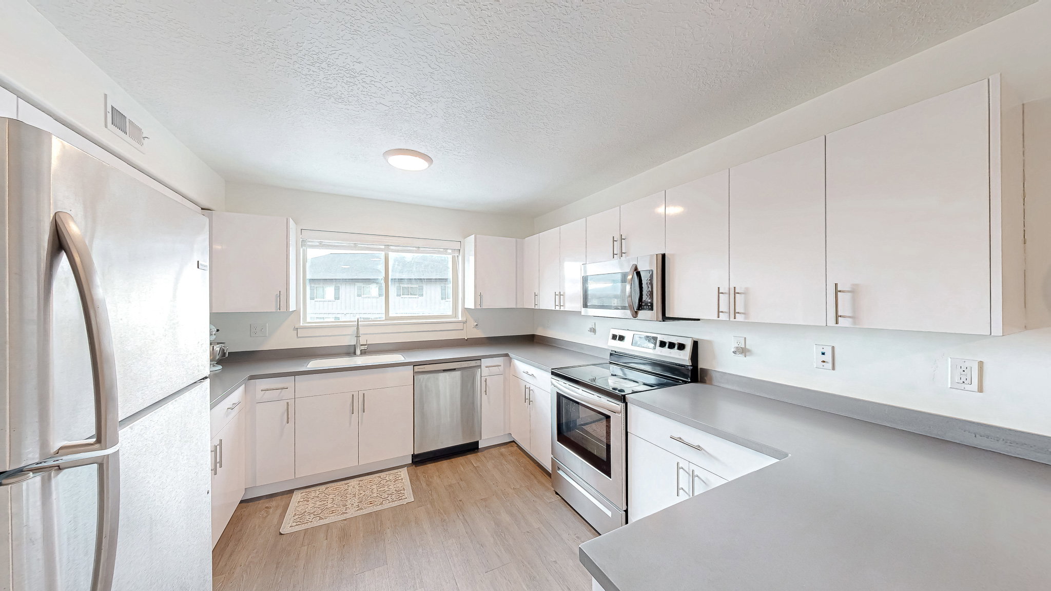 Kitchen with stainless steel appliances, a textured ceiling, white cabinets, light wood-type flooring, and light countertops