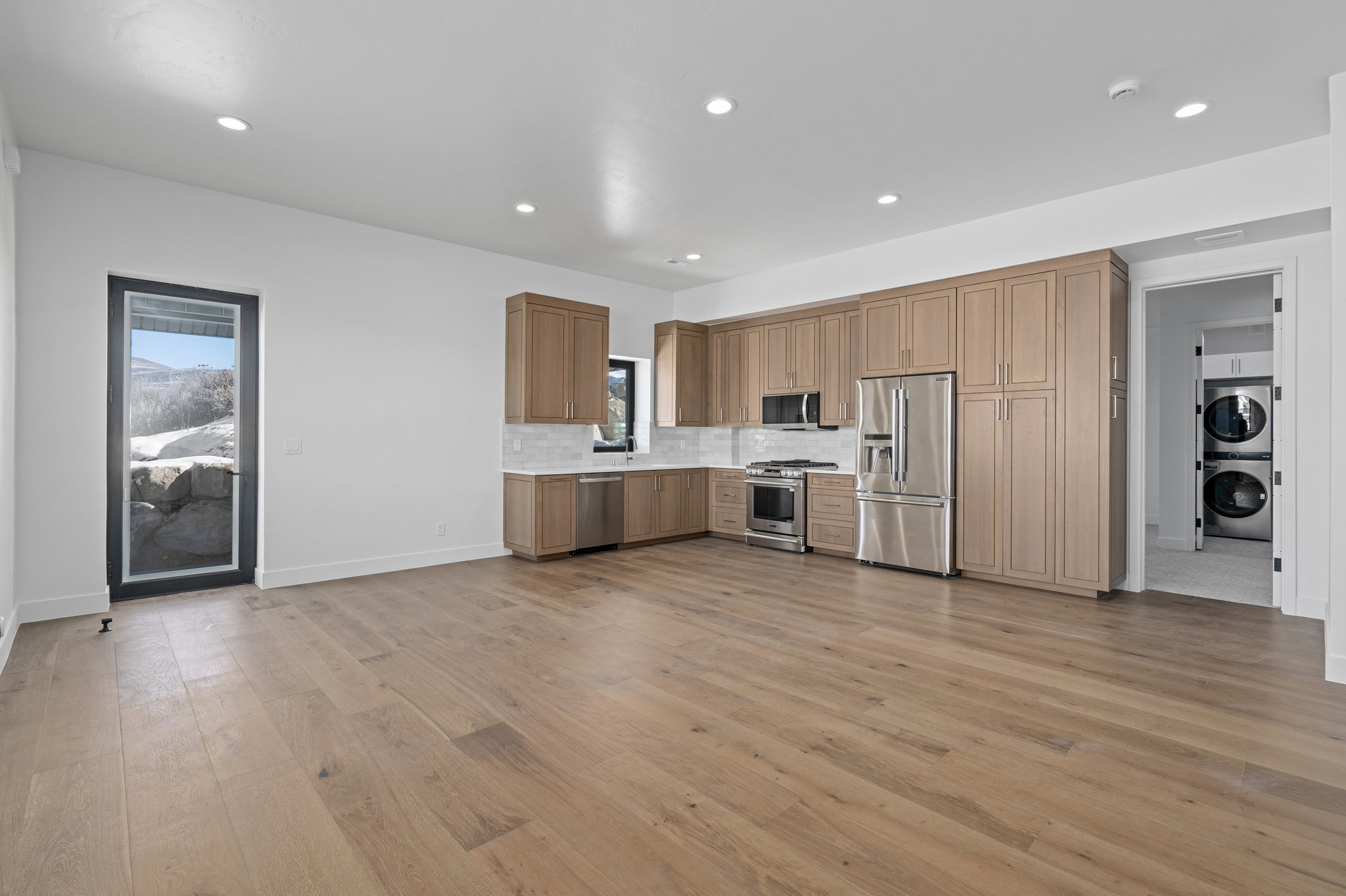 ADU Kitchen featuring stainless steel appliances, light countertops, stacked washer / dryer, tasteful backsplash, and light wood-style floors