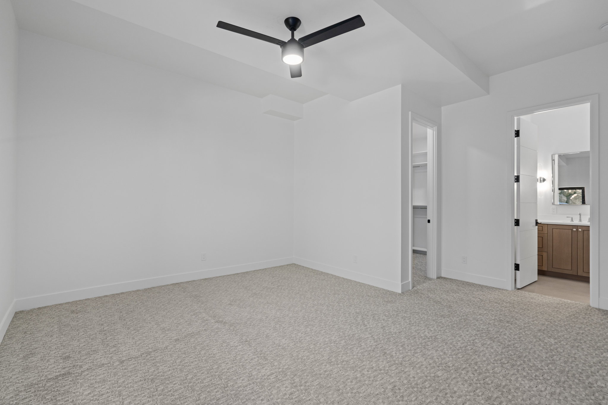 ADU bedroom suite with light carpet, a walk in closet, a ceiling fan, and ensuite bath