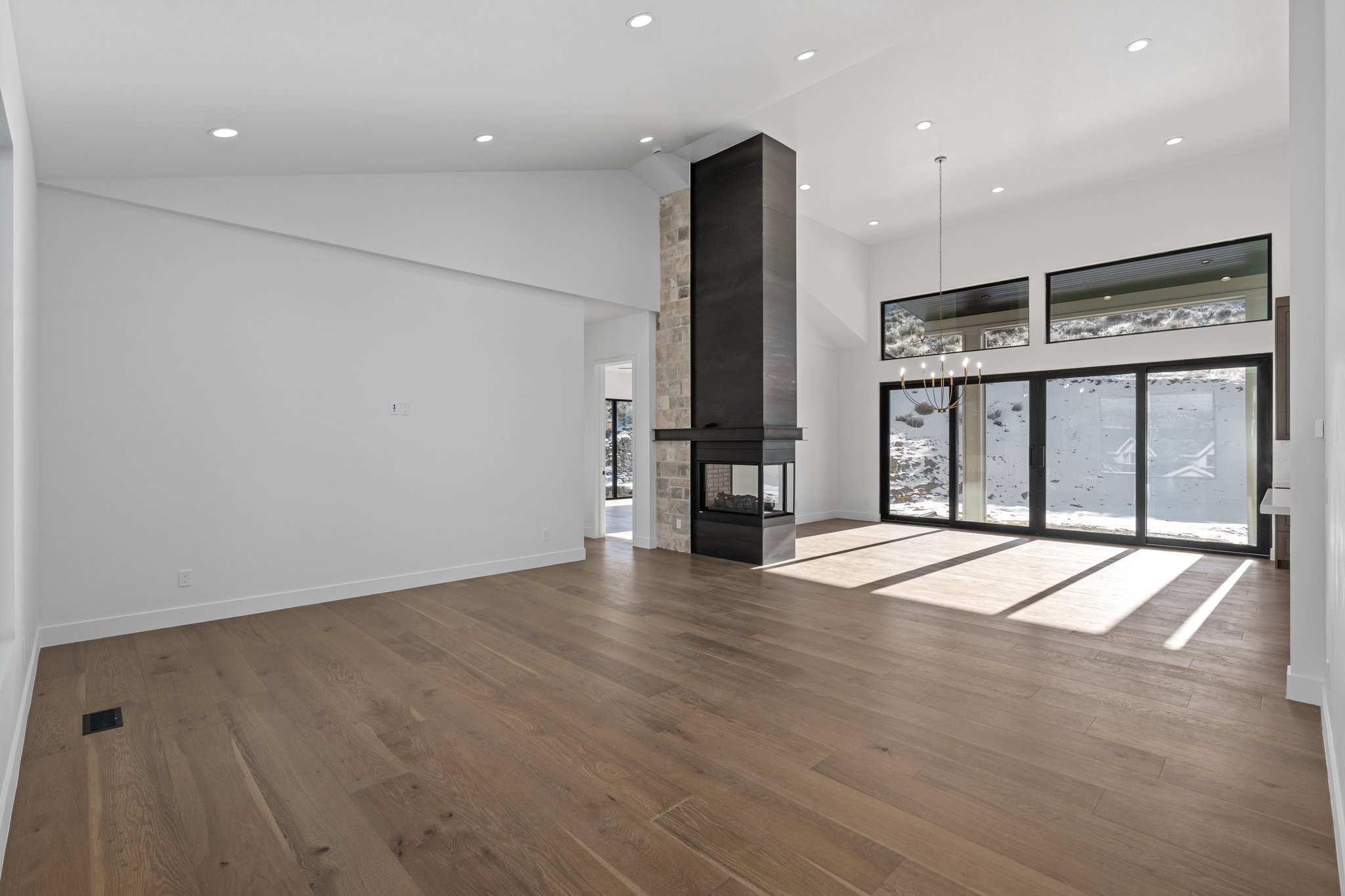 Unfurnished living room with lofted ceiling, dark wood finished floors, a multi sided fireplace, healthy amount of natural light, and hanging lights