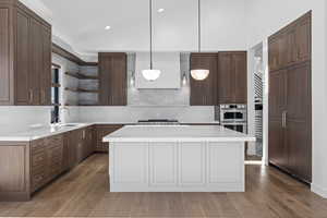 Kitchen featuring a center island, light stone counters, two tone cabinets, light wood-style flooring, and pendant lighting