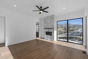 primary suite featuring light wood-style floors, a ceiling fan, a fireplace, a mountain view, and recessed lighting