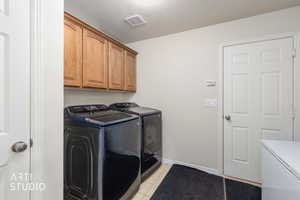 Laundry room with washing machine and clothes dryer, cabinet space, light tile patterned floors, and a textured ceiling