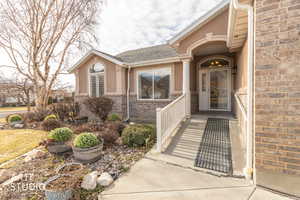 View of exterior entry featuring brick siding, a shingled roof, and stucco siding