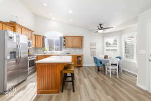 Kitchen featuring wood finish cabinets, stainless steel appliances, vaulted ceiling, a kitchen island, and a breakfast bar