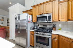 Kitchen with stainless steel appliances, light countertops, ornamental molding, arched walkways, and vaulted ceiling