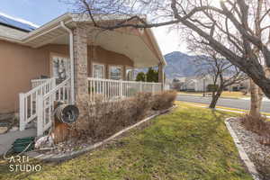 View of side of home featuring stucco siding, covered porch, a yard, a mountain view, and a residential view