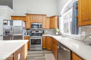 Kitchen featuring stainless steel appliances, light countertops, wood finish cabinetry, light wood-style floors, and tasteful backsplash