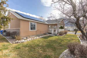 View of property exterior featuring solar panels, stucco siding, a yard, and roof with shingles