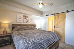 Bedroom featuring dark carpet, a barn door, a ceiling fan, and wallpapered walls